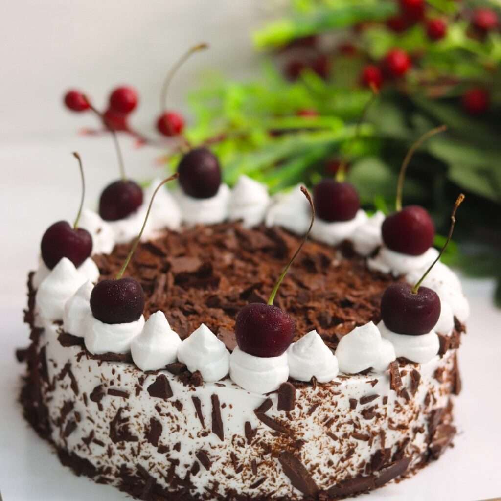 A rich chocolate cake known as 'Black Forest Cake,' featuring whipped cream and cherries, topped with chocolate shavings and whole cherries.