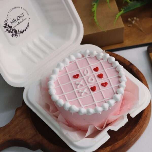 A pink bento cake with white design and heart sprinkles