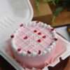 A pink bento cake with white design and heart sprinkles