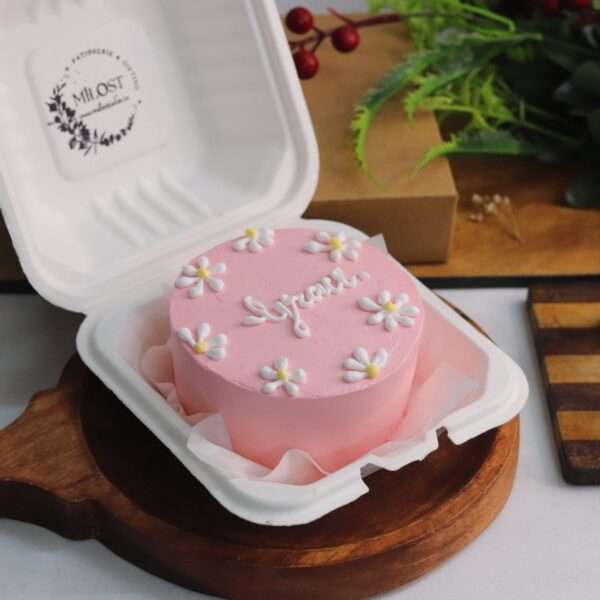 A pink bento/lunch box cake with white and yellow flower design