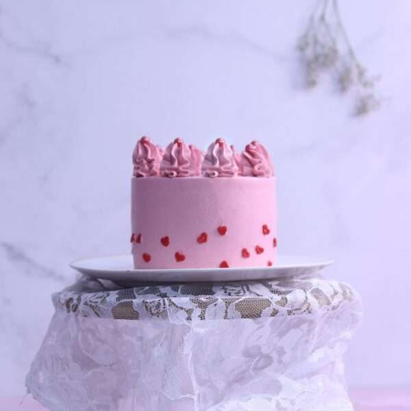 A pink tall cake with heart sprinkles