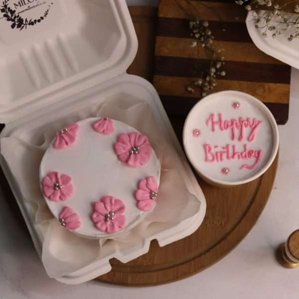 A white bento cake with a pink floral design and a cup dessert